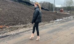 A girl in transparent high-heeled boots with exposed toes walks through deep mud