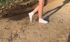 A girl in white socks walks along a dusty road and then she plunges them into the mud where they get dirty entirely