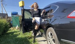 A girl in high-heeled boots poses, presses the pedals of a car, plays with boots