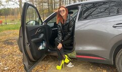 A girl in very high-heeled shoes is playing with a car in the woods, she really likes to pedal and play with shoes